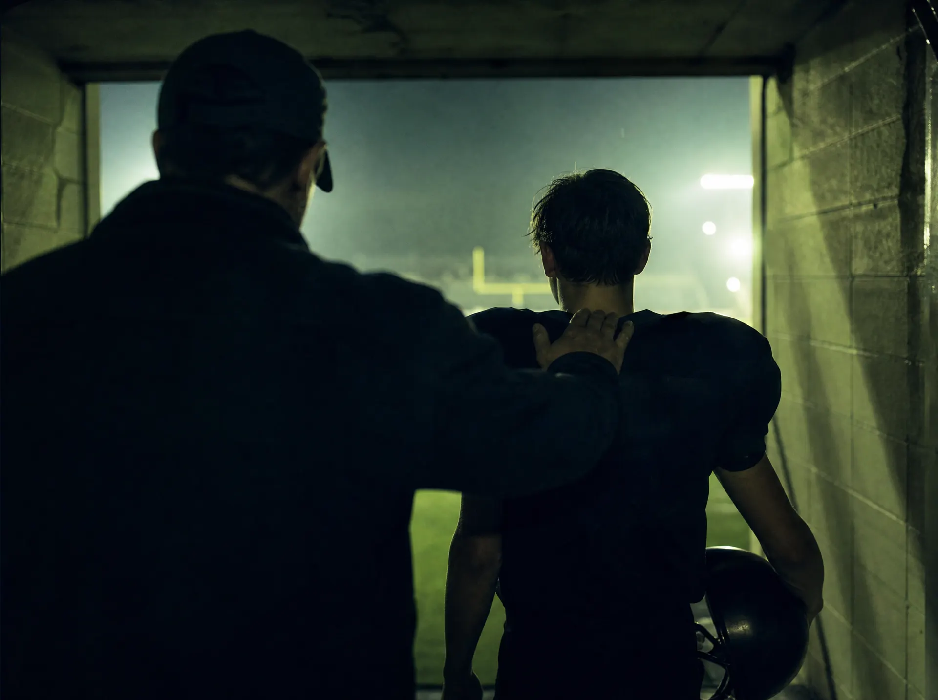 A mentor's hand on a young player's shoulder as he walks out of the tunnel toward the field